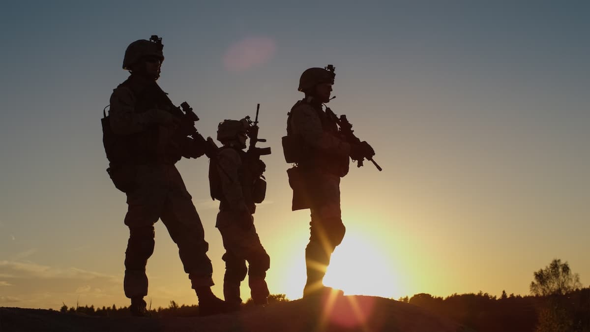 Squad Of Three Fully Equipped And Armed Soldiers Standing On Hill In Desert Environment In Sunset Light Squad Of Three Fully Equipped And Armed Soldiers Standing On Hill In Desert Environment In Sunset Light