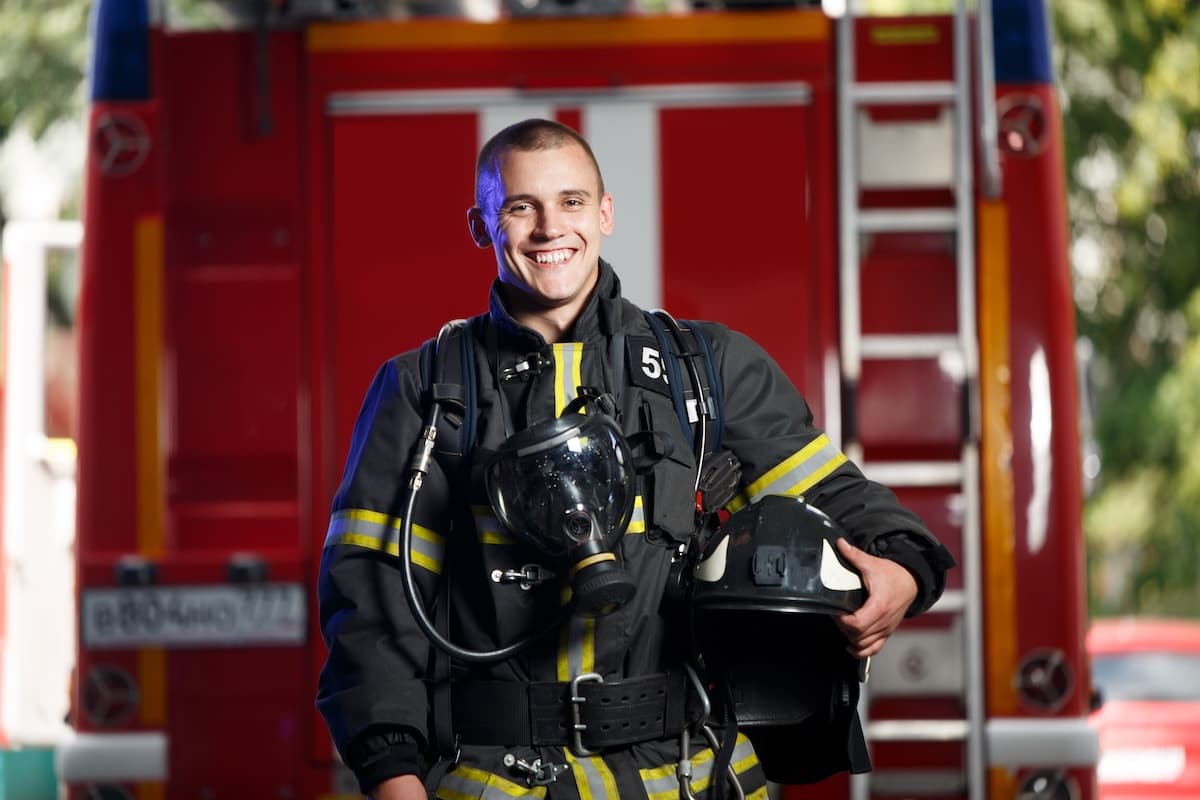 Happy Fireman With Gas Mask And Helmet Near Fire Engine Happy Fireman With Gas Mask And Helmet Near Fire Engine